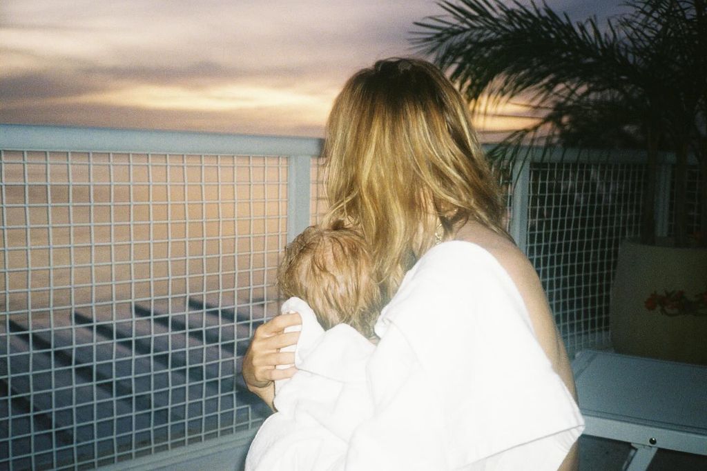 suki waterhouse holding daughter with their backs to the camera