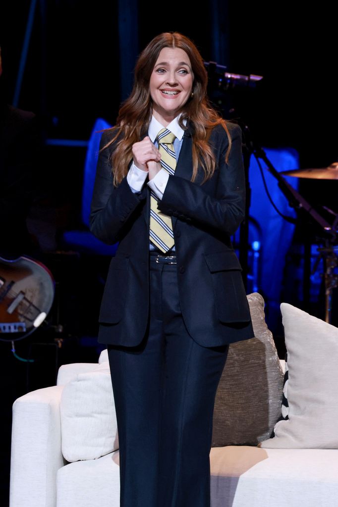 drew barrymore clasping hands together on stage and smiling