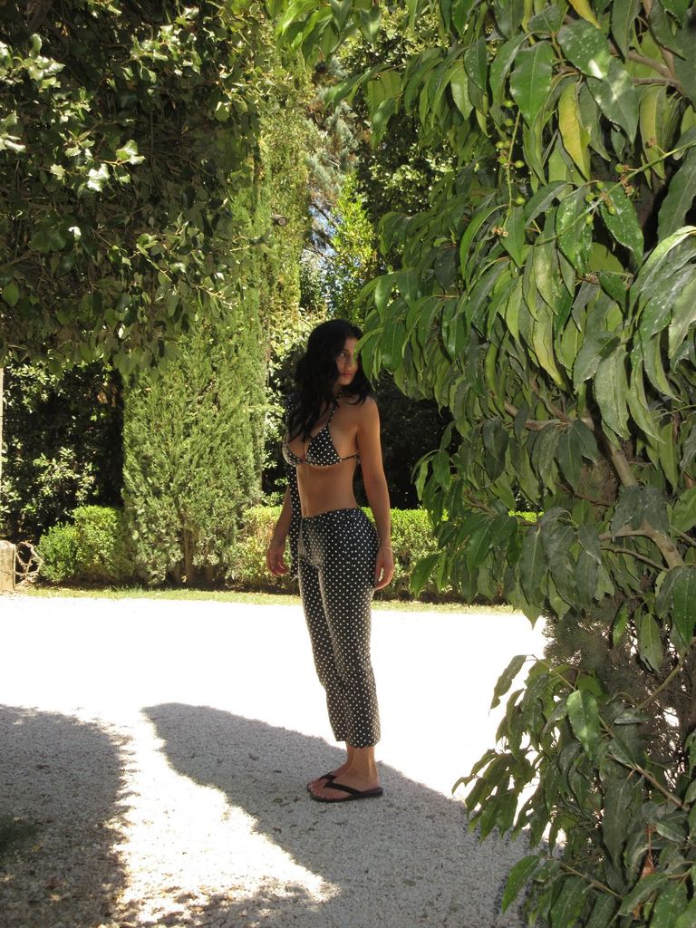 Kylie Jenner looks away from the camera in her polka dot bikini top and trousers. Lush green leaves surround her and the sun is shining