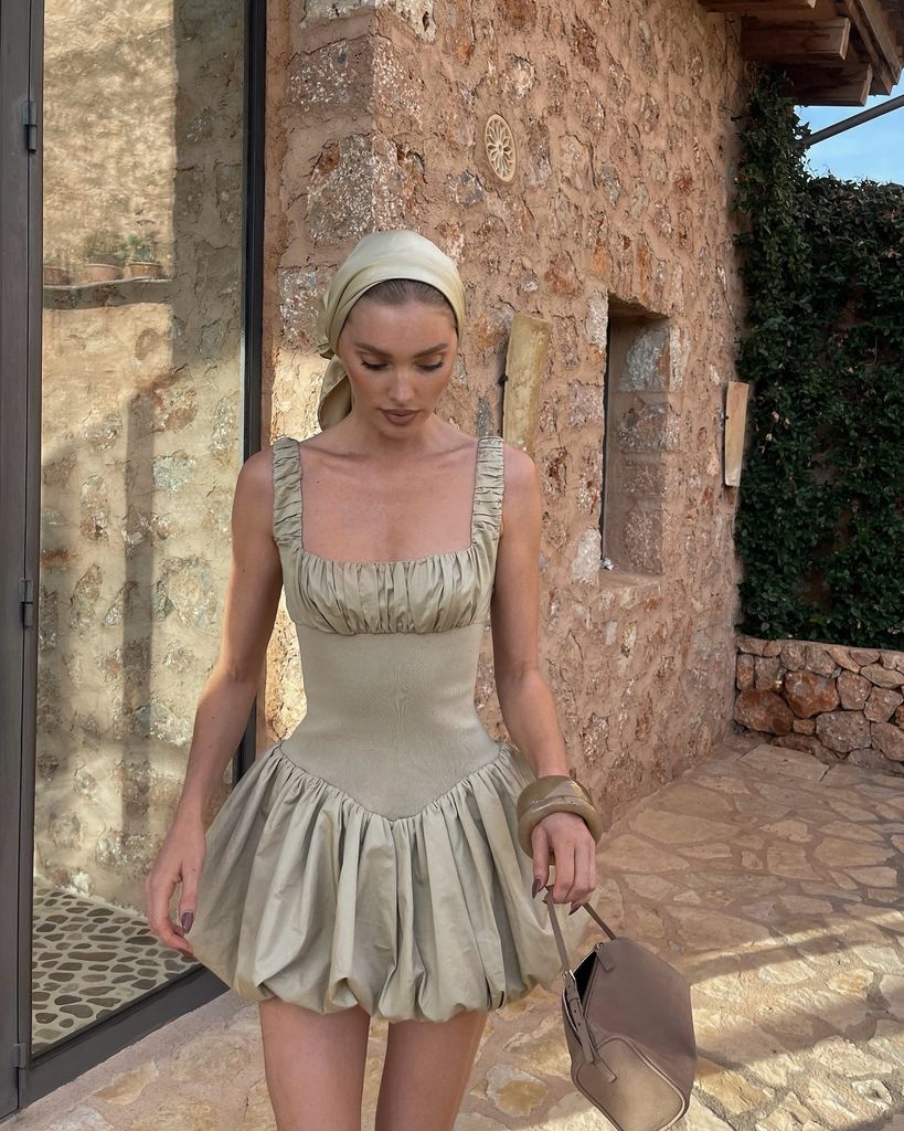Elsa Hosk looks down and walks towards the camera in her drop waist ruched mini dress with matching accessories