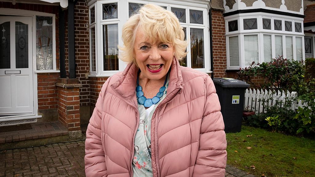 woman in pink coat standing outside house