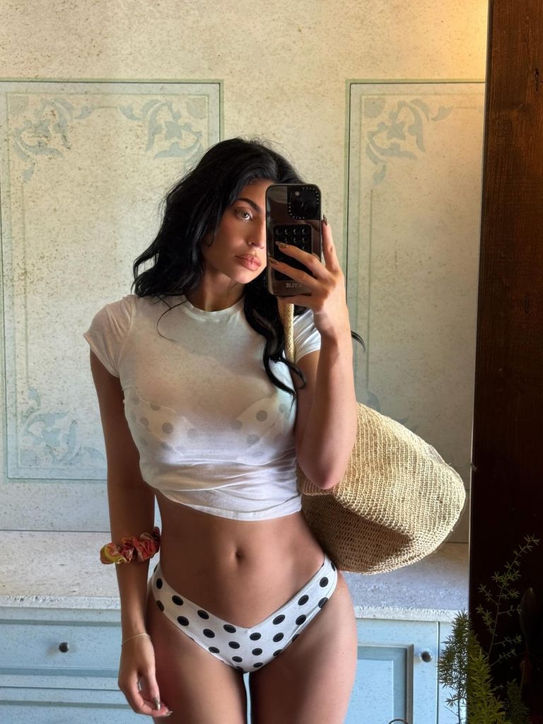 Kylie Jenner takes a mirror selfie wearing a white polka dot bikini with black pots and a white t-shirt