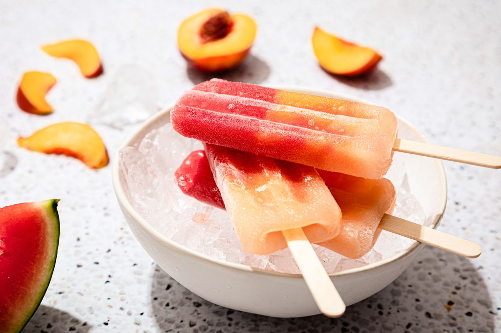 Homemade ice cream popsicles in a bowl with ice, made with watermelon and peach, under hard light.