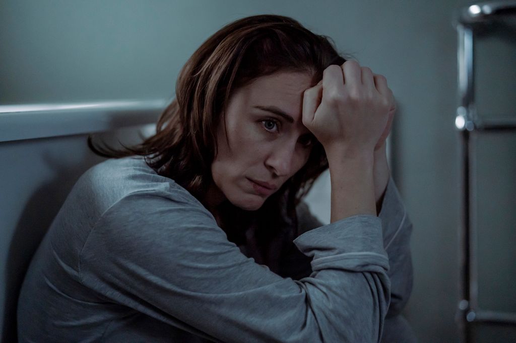 woman sitting in bathroom with hands on forehead