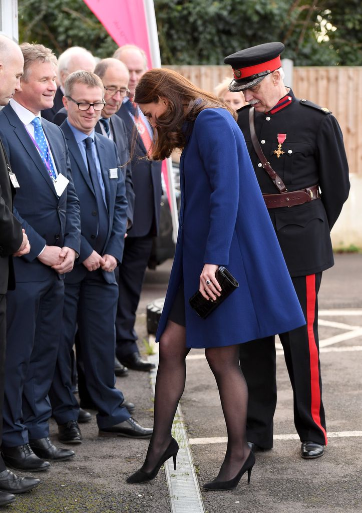 Kate in blue coat with heel stuck in a grate