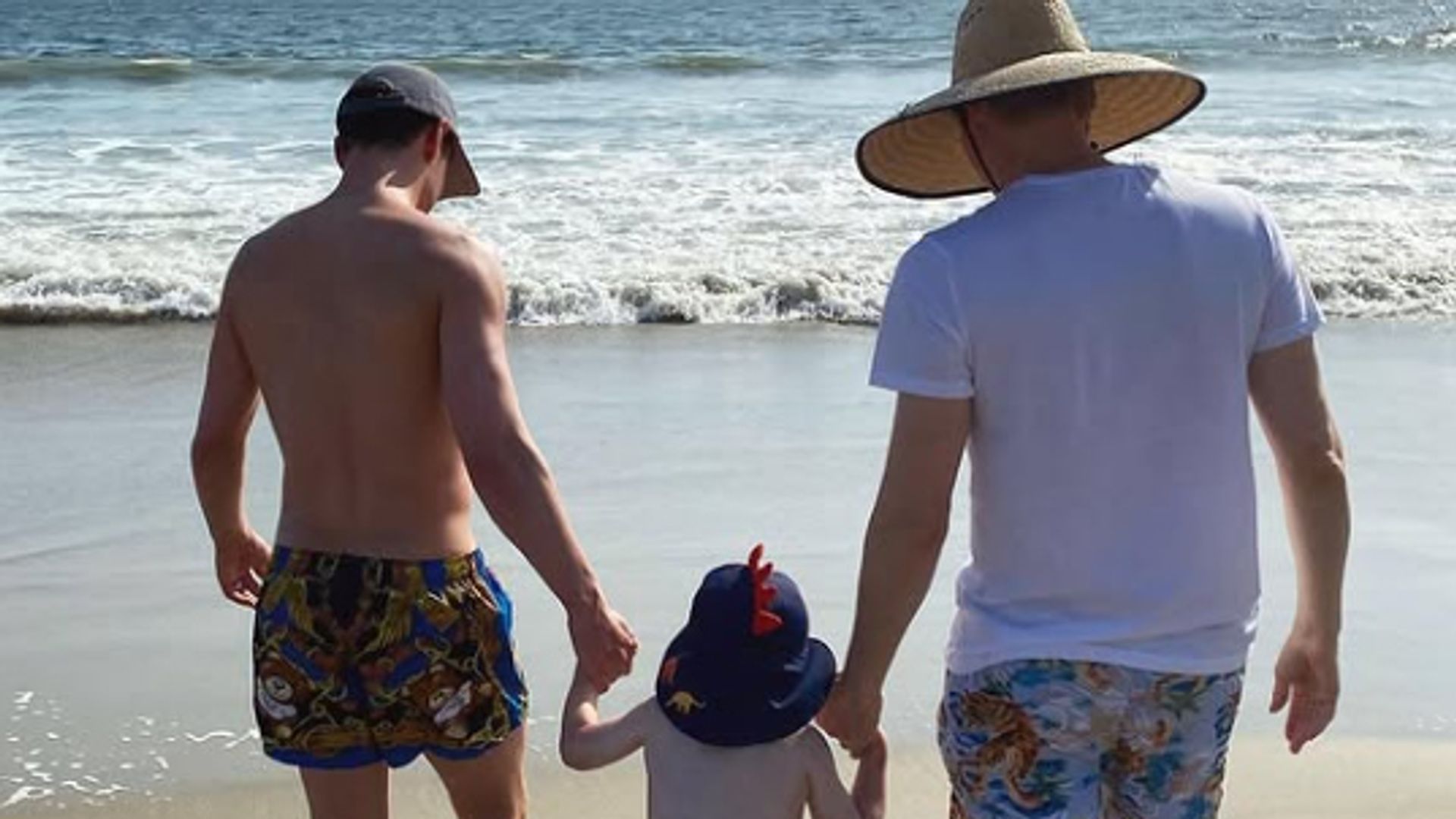 Tom Daley and Dustin Lance Black walking on the beach with their son Robbie