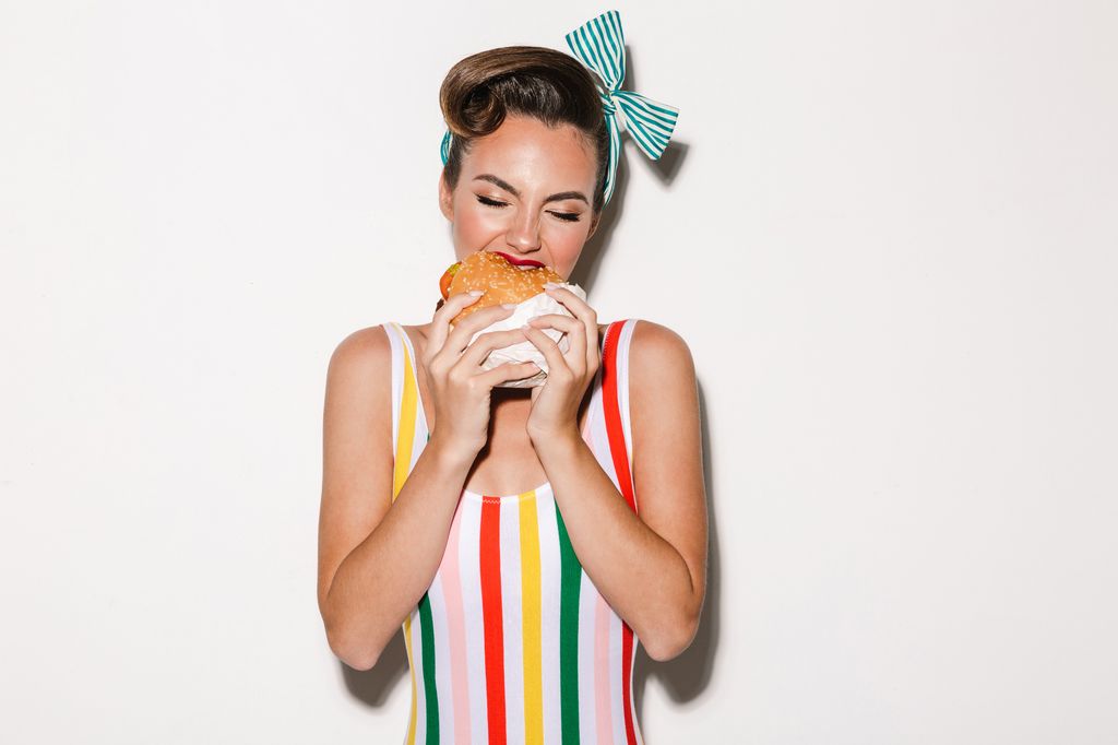 Photo of pretty pin up woman isolated over white wall background eating burger