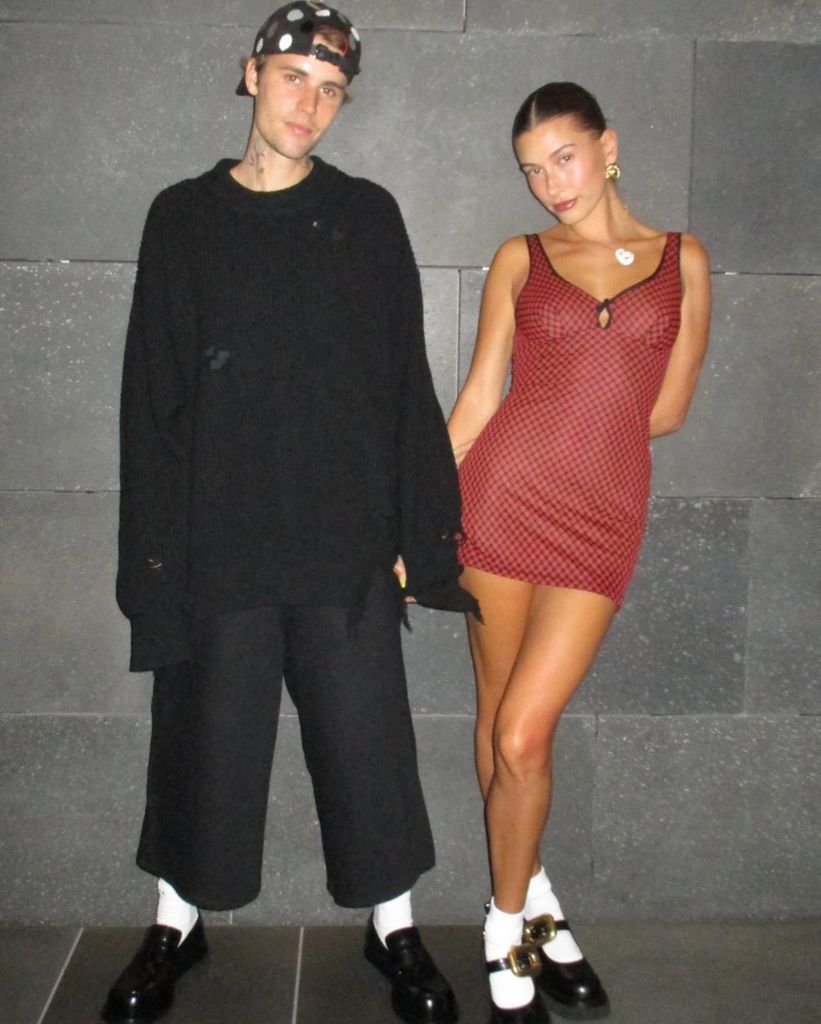 justin and hailey bieber standing in front of brick wall holding hands