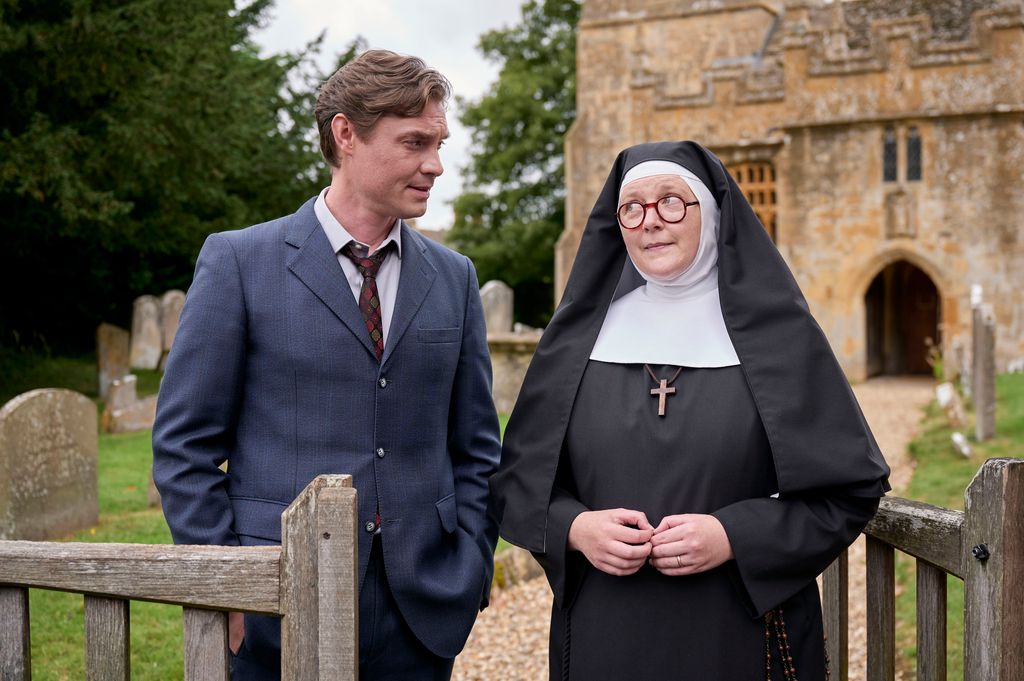 man in suit standing next to nun in front of church