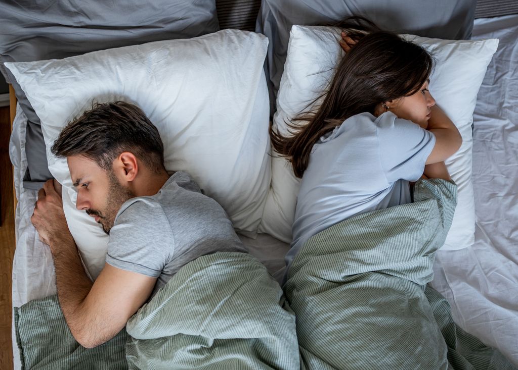 Young couple is lying back to back in bed, having relationship problems and feeling estranged after having a fight