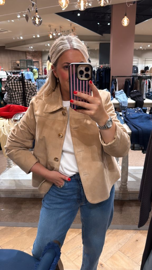 Shopping editor Leanne Bayley wearing the River Island premium suede jacket posing in front of a mirror. She is styling it with jeans and a white t-shirt