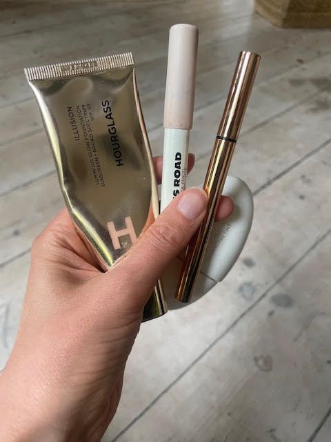 Cassie's is holding her favourite products; two skin tints by Hourglass and Lisa Eldridge and an eyeliner by Sculpted by Aimee