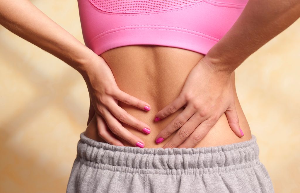 woman in pink crop top with her hands on her back