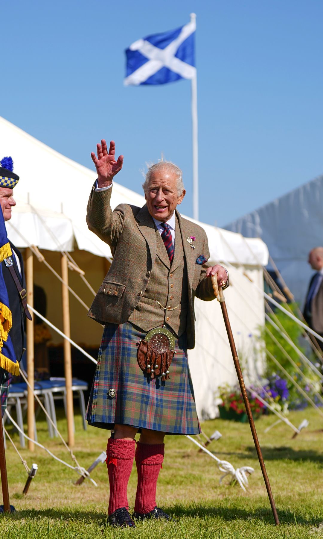 King Charles waving at people in front of the Scottish flag