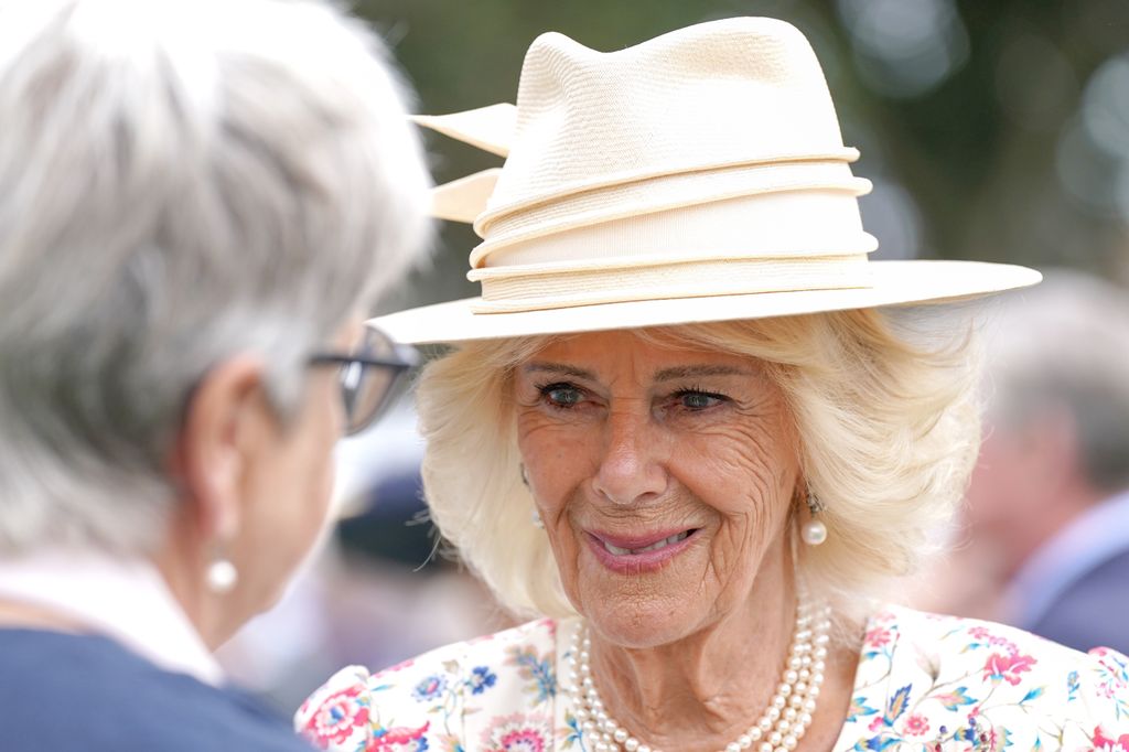 Queen Camilla smiling in floral dress, hat and pearls