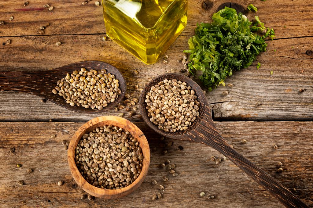 Hemp seed in wooden spoons and oil on rustic wooden table