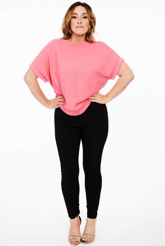 Grace with hands on hips in black skinny jeans and coral top