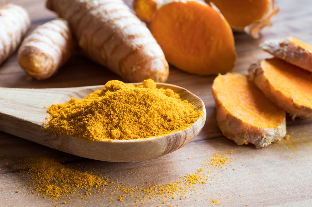 Turmeric powder with fresh turmeric root in the background