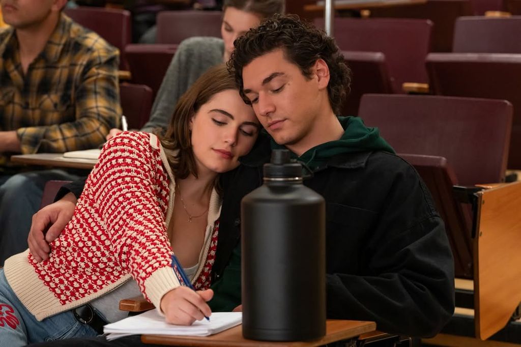 Two people sit together while one writes on paper