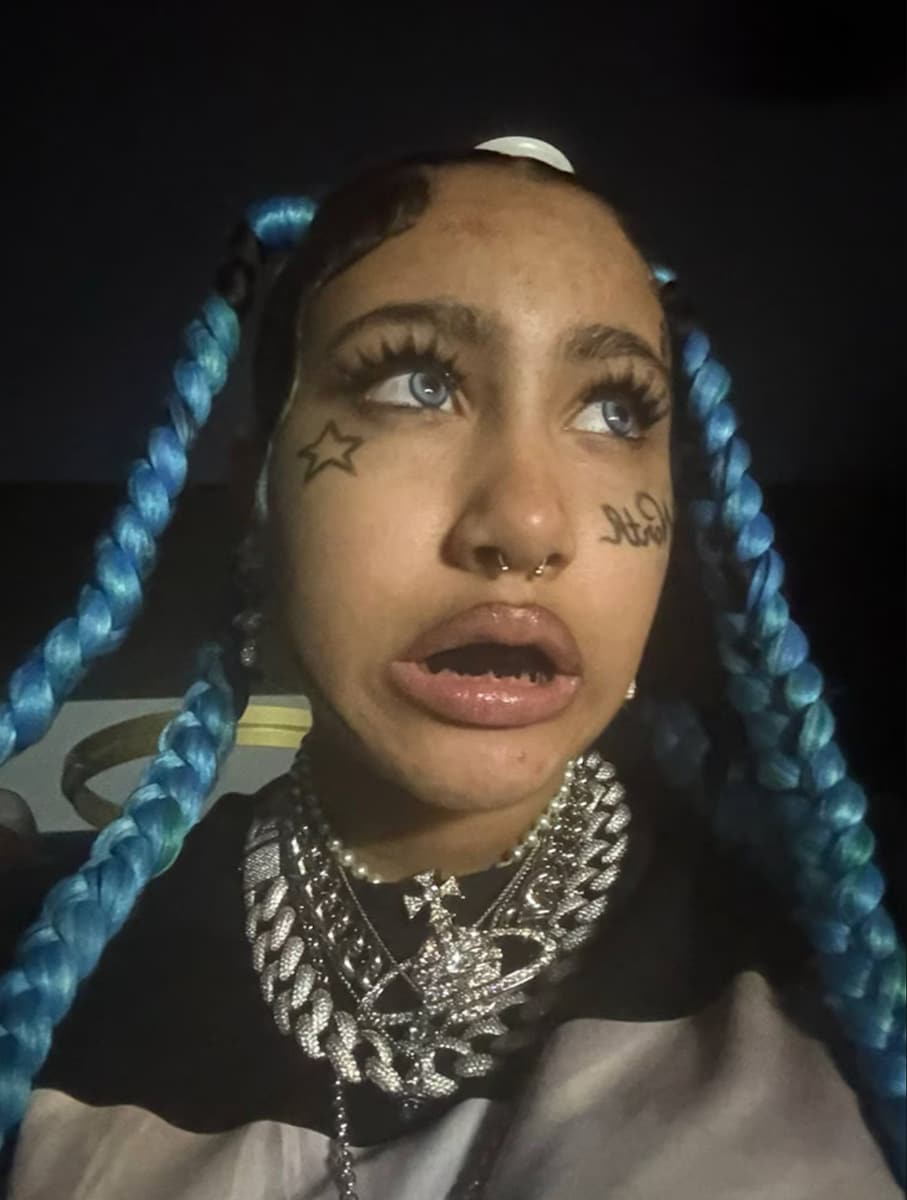 Her new look features a striking mix of edgy and playful, complete with fake face tattoos, icy-blue contact lenses, and a faux septum piercing.