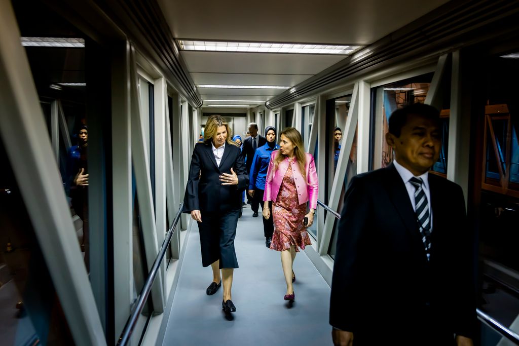 Queen Maxima walking through airline tunnel talking with woman