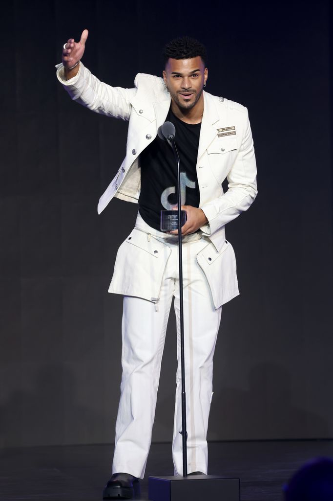 Jeremiah Brown accepts the Rising Star of the Year Award on stage at the TikTok awards. He wears a white suit with oversized white pockets and black t-shirt.