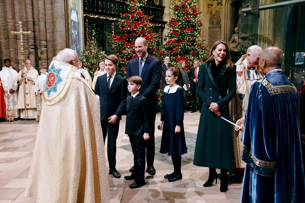The Prince and Princess of Wales and their children Prince George, Prince Louis (centre) and Princess Charlotte talking to priest in abbey in front of christmas tree
