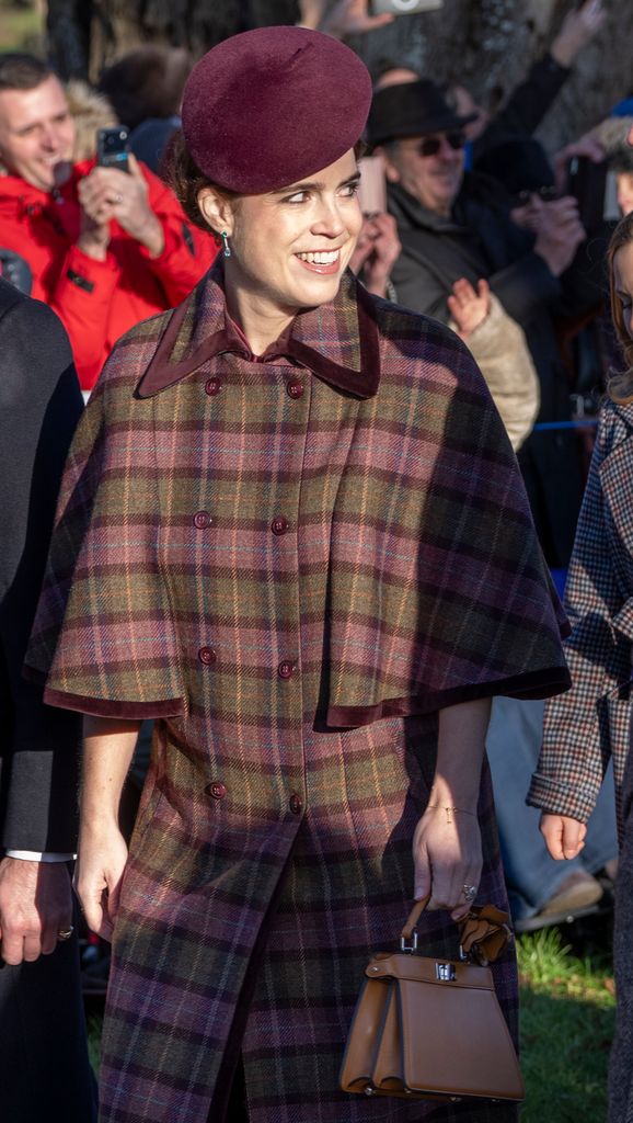 Princess Eugenie at Sandringham wearing a burgundy coloured hat and plum and green checked caped coat