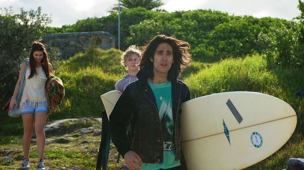 Two men and a woman walking down to a beach, one of them carries a surfboard