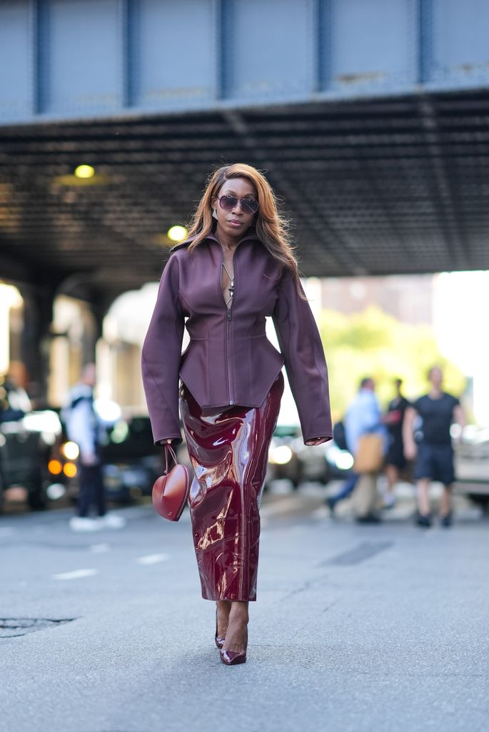 A fashion week guest wears a burgundy top, burgundy latex pencil skirt and a heart shaped bag