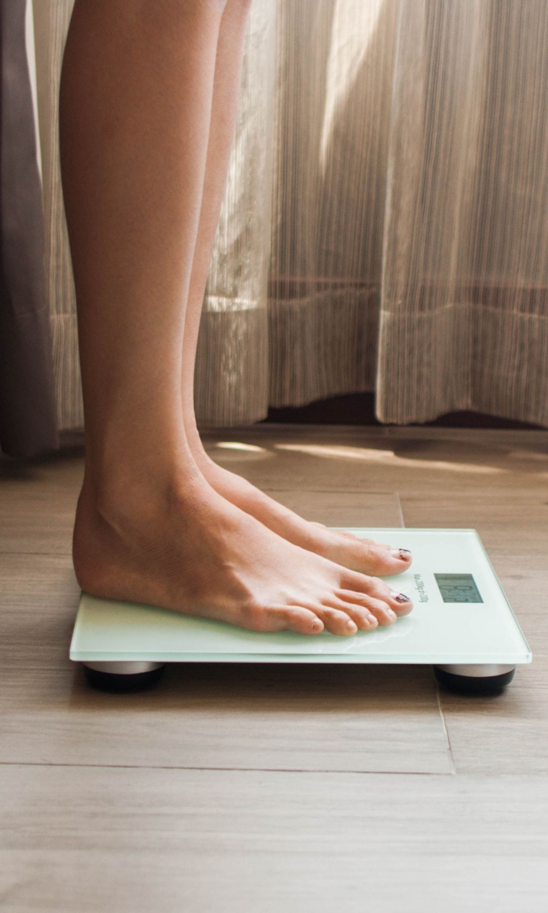 A low-angle view of a young woman who is weighing herself in a weighing scale