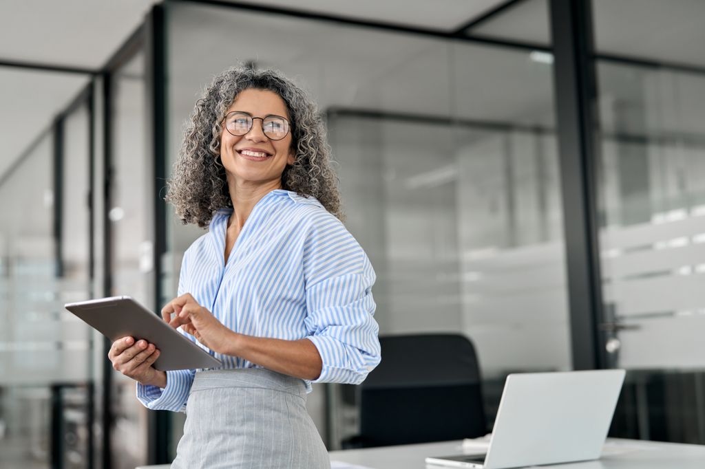 Stylish professional woman with grey curly hair in an office with a tablet