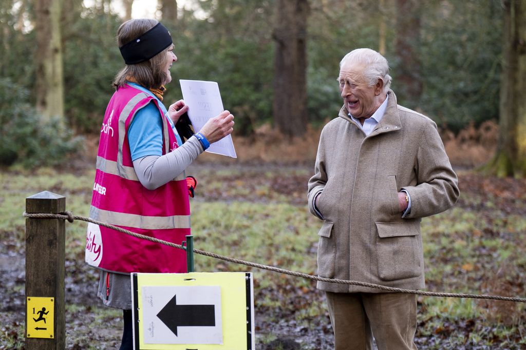 King Charles III looks at a sign held by Sarah Byatt at a marshal point of the Sandringham parkrun in Sandringham, Norfolk