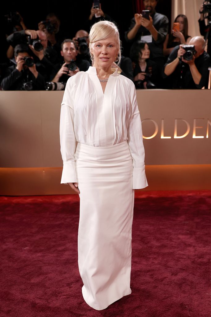 Pamela Anderson on red carpet in long white shirt dress