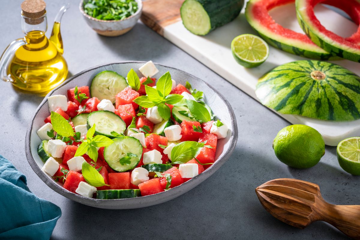 Healthy vegetarian watermelon salad bowl with feta cheese, cucumber and parsley on gray background with cutting board and olive oil, Mediterranean diet 