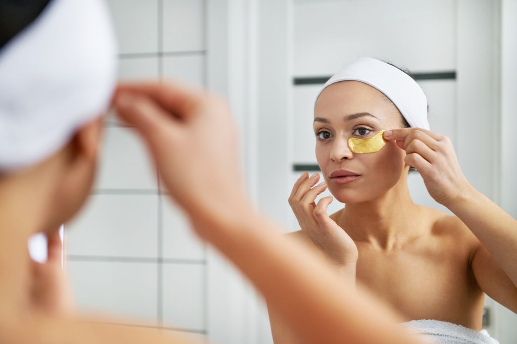Woman in bathroom applying gold under eye mask
