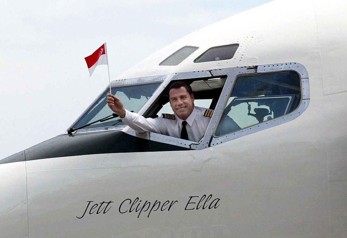 John Travolta waves a Singaporean flag from the Qantas Boeing 707 cockpit window upon arriving at Singapore International Changi Airport.