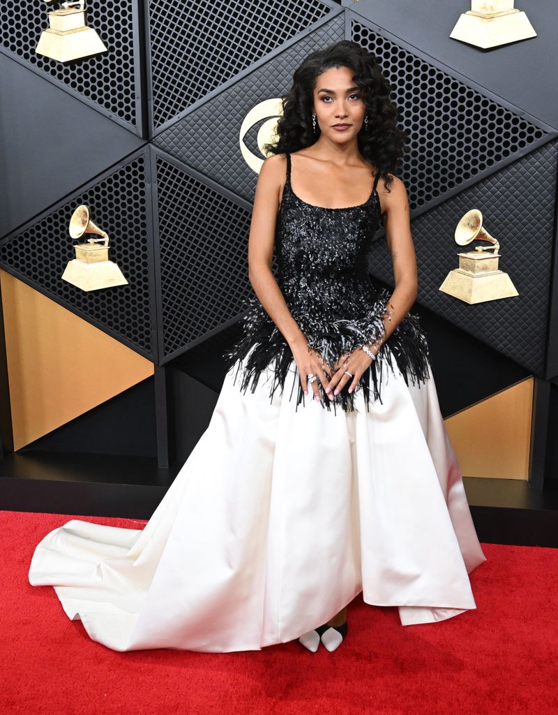 Olivia Dean wearing dress with a full white skirt and black sequin top, with sequin fringed edge