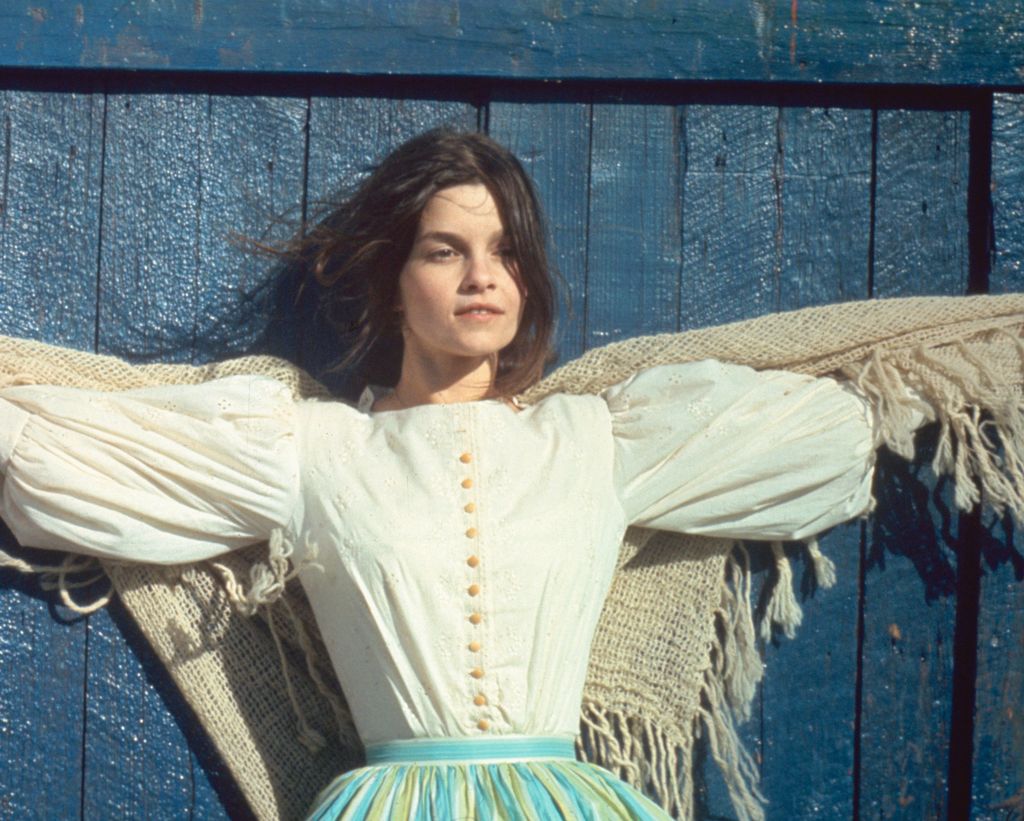 Still of Genevieve Bujold in a white blouse in front of a blue wall in Kamouraska