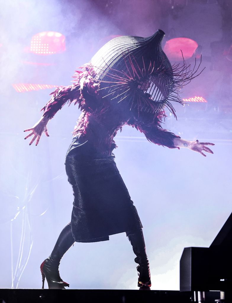 Lady Gaga performs on stage in a leather pencil skirt, beaded top and cage headpiece