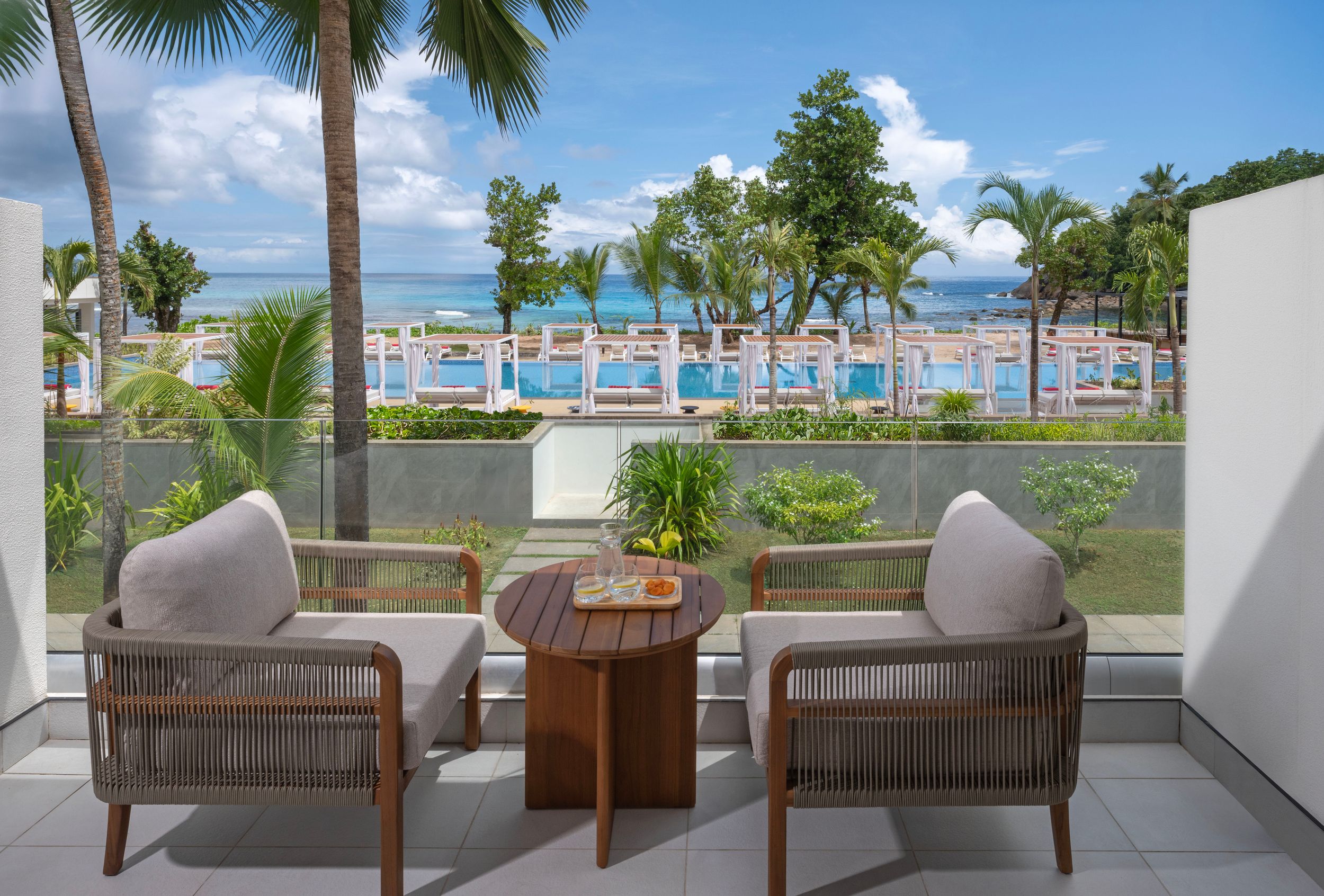 A superior ocean view room balcony with a table and chairs overlooking a pool and the sea in the horizon