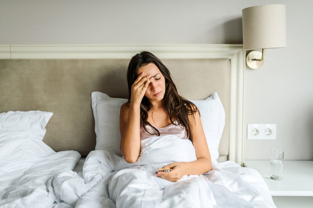 woman lying in bed, feeling unwell, with her hand on her head