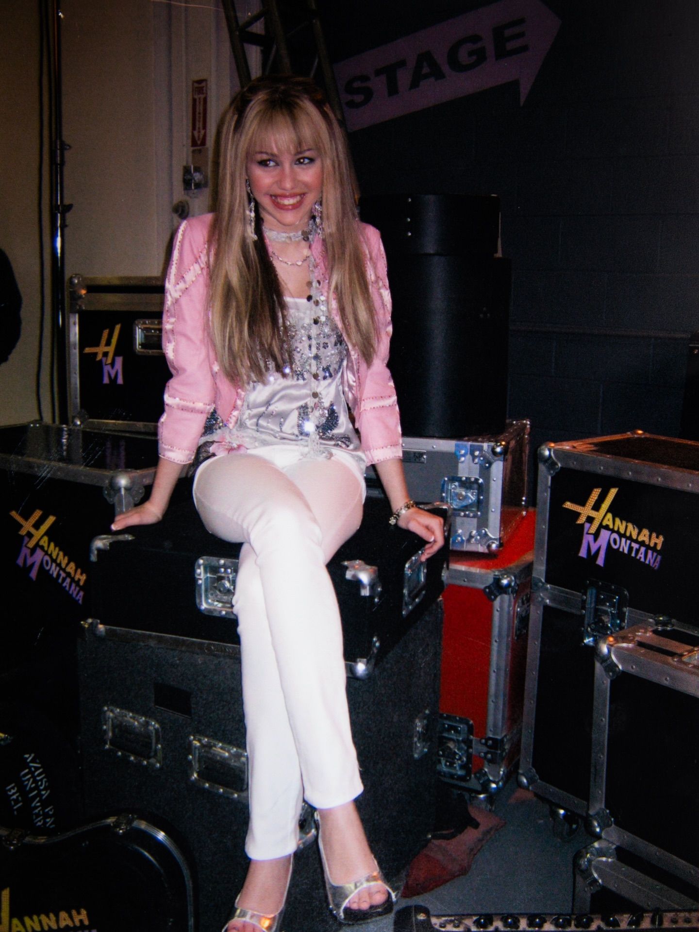Miley Cyrus dressed as Hannah Montana sitting on an amp 