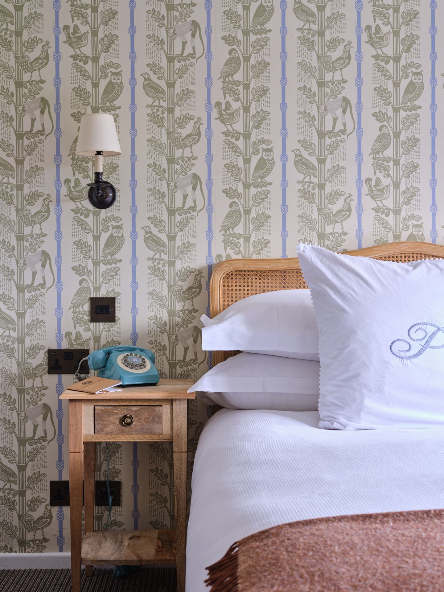 A bedroom at The Painswick with floral wallpaper, white bedding and a deep pink blanket draped on the bed