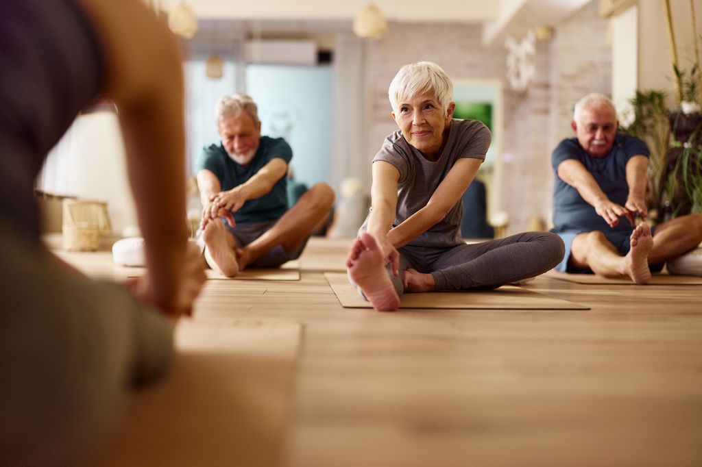 Group of mature people doing stretching exercises with their coach during a Yoga class in a studio 