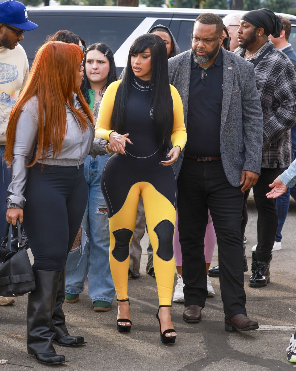 
Cardi B made a stunning entrance at the 2026 Fanatics Super Bowl Party in San Francisco. She confidently moved through the crowd wearing an eye-catching black and yellow one-piece jumpsuit with a sporty, futuristic design.