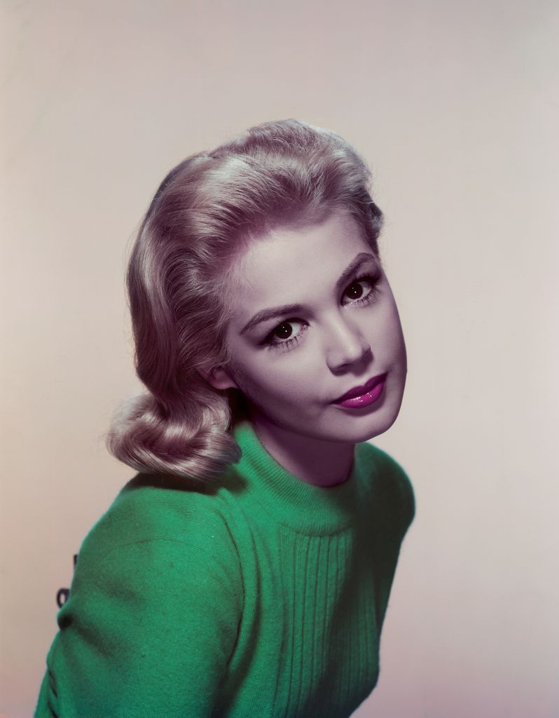 Sandra Dee sits looking at the camera in a green jumper with a forceful gaze to the camera.