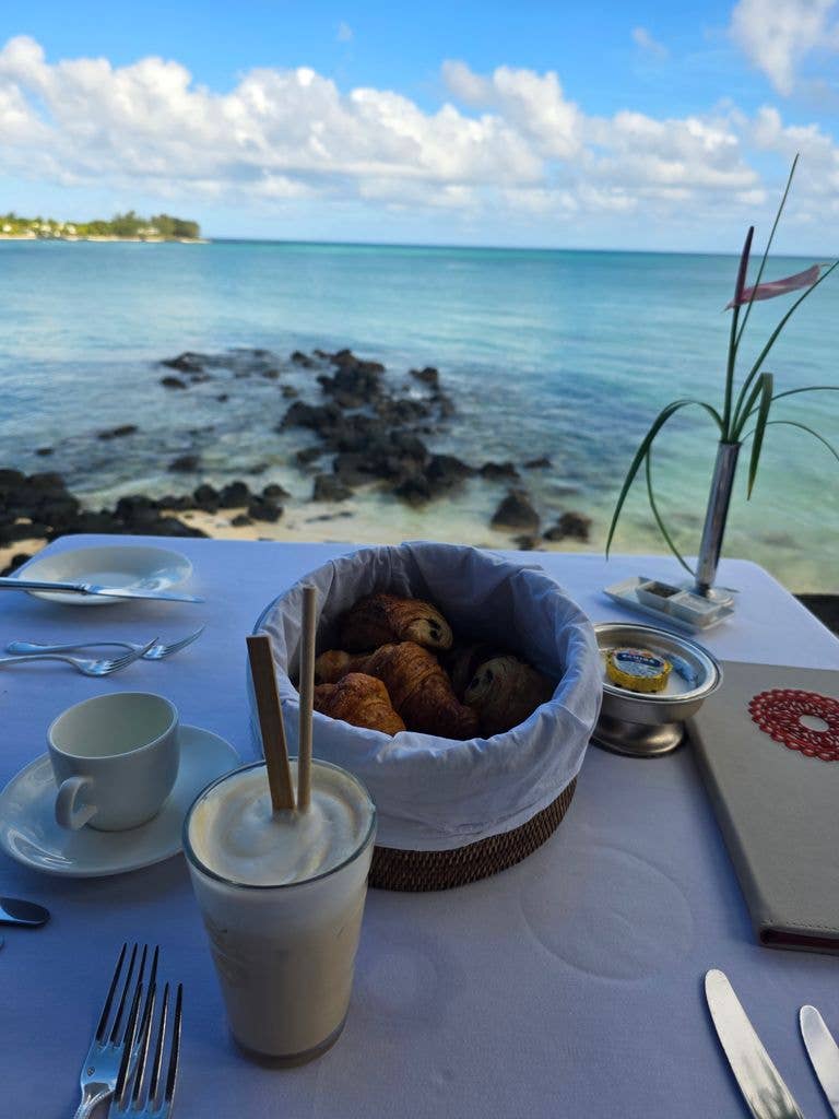 A view of the sea, with croissants in a bowl and an iced coffee laid out on a breakfast table in Mauritius
