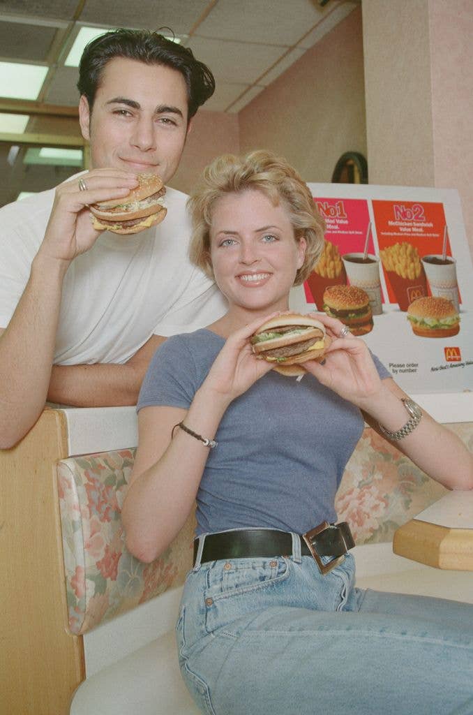 A couple hold up McDonalds burgers in tshirts and jeans.