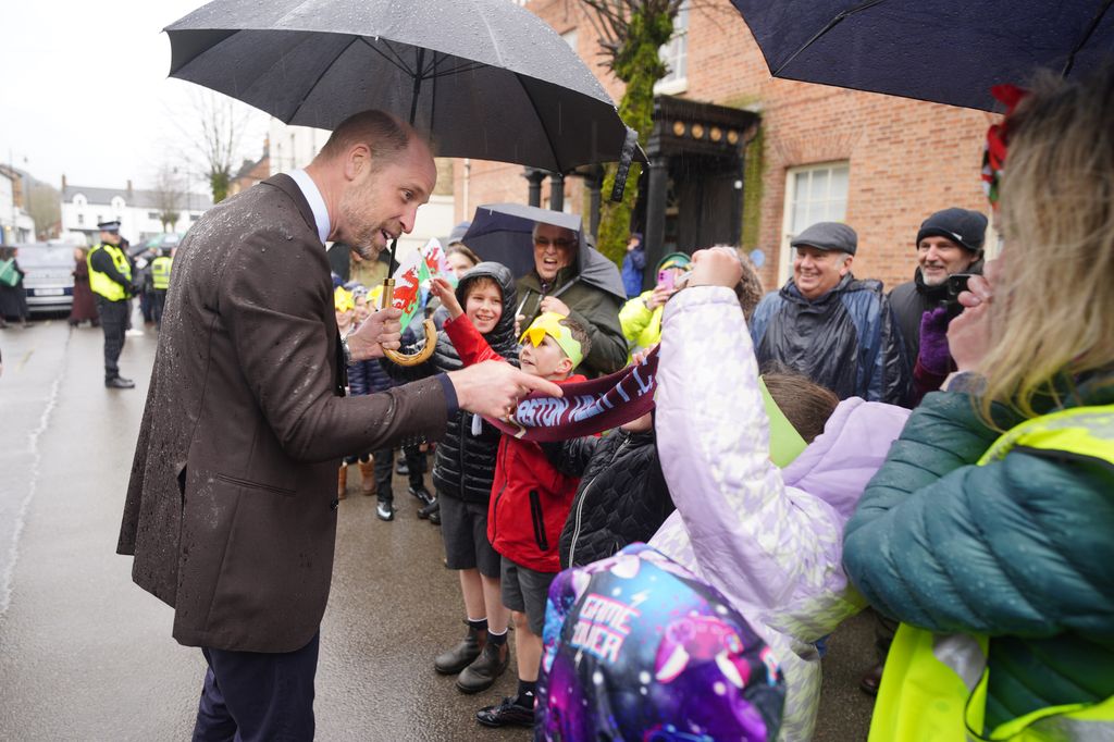 Prince William, Prince of Wales, shelters from the rain under an umbrella whilst meeting members of the public during a visit to the Hanging Gardens, a space dedicated to nurturing community resilience and creativity, on February 26, 2026 in Newtown, Wales